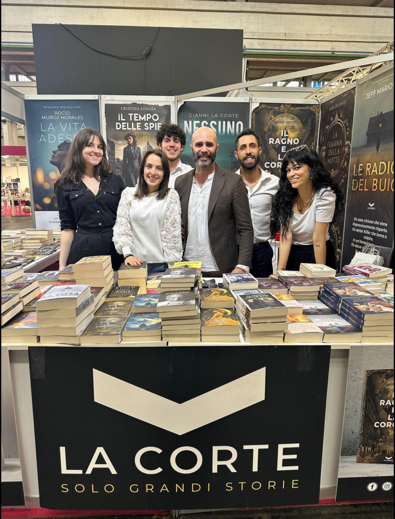 A publisher's booth at the international book fair, with the staff in the middle and posters of book covers behind them.